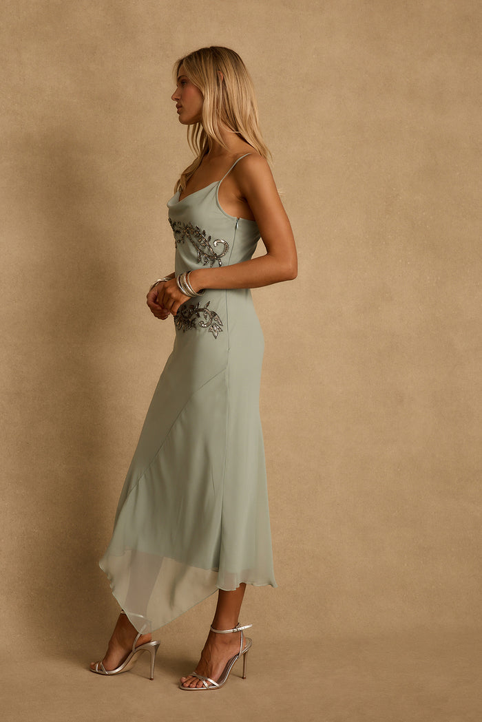 Side profile of the Amelie beaded chiffon midi dress with silver heels, a resort evening look.