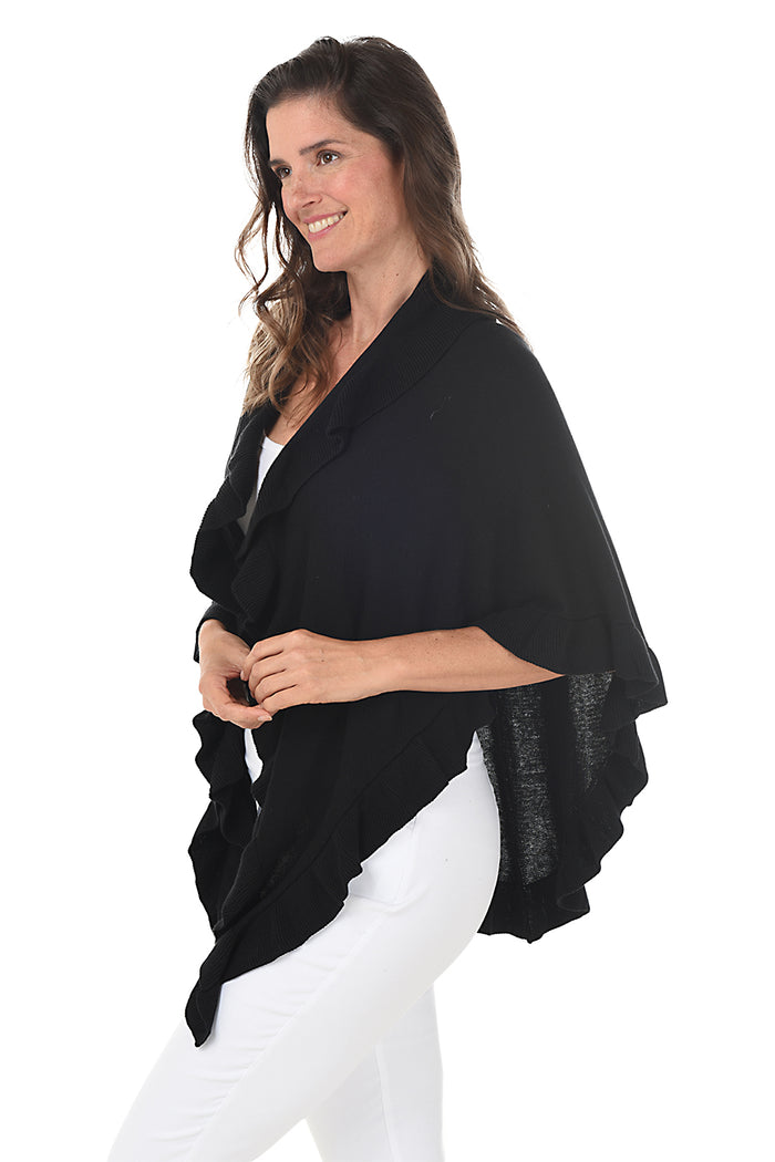 A woman wearing a black open front wrap sweater with ruffled rib-knit trim over a white top and white pants. Side shot.