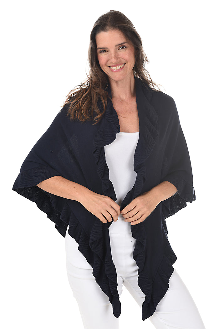 A woman wearing a navy open front wrap sweater with ruffled rib-knit trim over a white top and white pants.