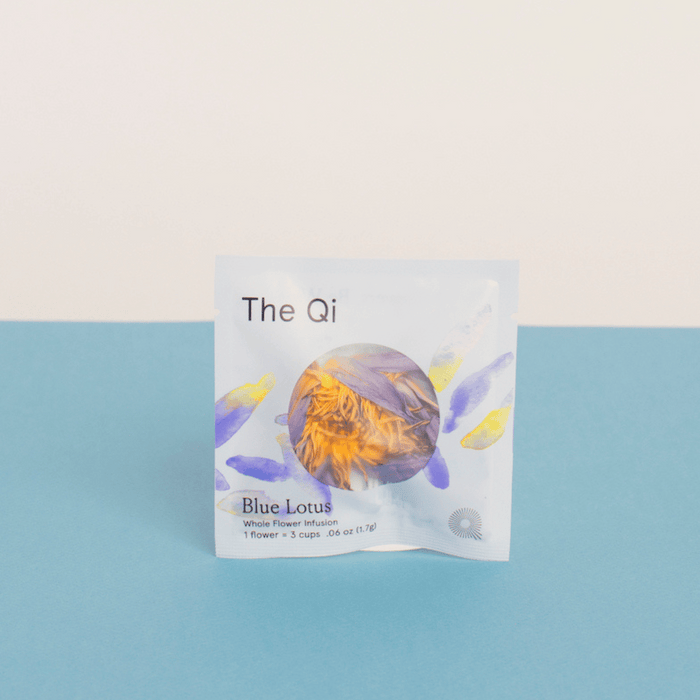 Packaging of Blue Lotus Whole Flower Tea | The Qi featuring a white packet with blue and yellow floral design accents, placed against a blue and light beige background.