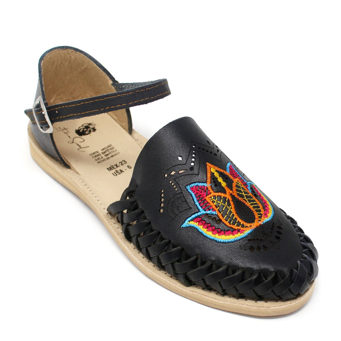 Women's handmade black genuine leather huarache sandals featuring colorful floral embroidery, woven leather detailing, adjustable ankle buckle strap, cushioned leather footbed, and authentic artisan craftsmanship made in Mexico.