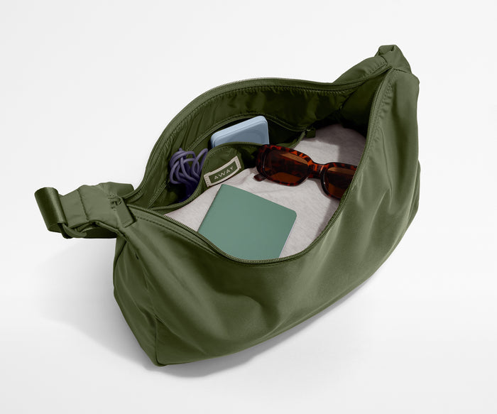 Green bag with items like sunglasses and a phone on a white background