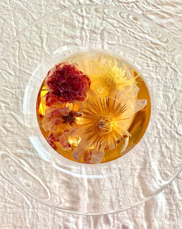 Close-up top view of a glass bowl filled with infused floral tea featuring vibrant yellow and deep red flowers, showcasing the Floral Collection (Variety Box) | The Qi for skincare and wellness.