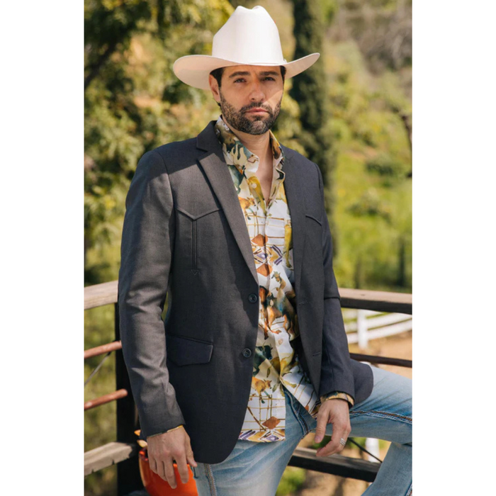 Man wearing a gray blazer, colorful shirt, and white cowboy hat outdoors.
