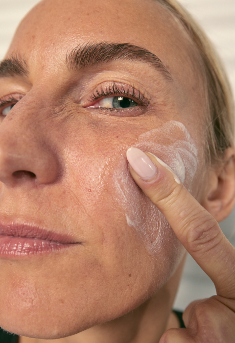 a close-up of a woman applying cream on her face