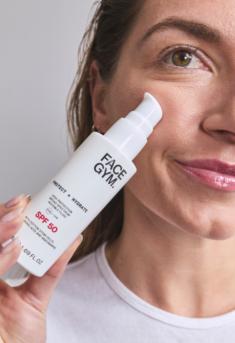 a woman holding a white bottle of face cream