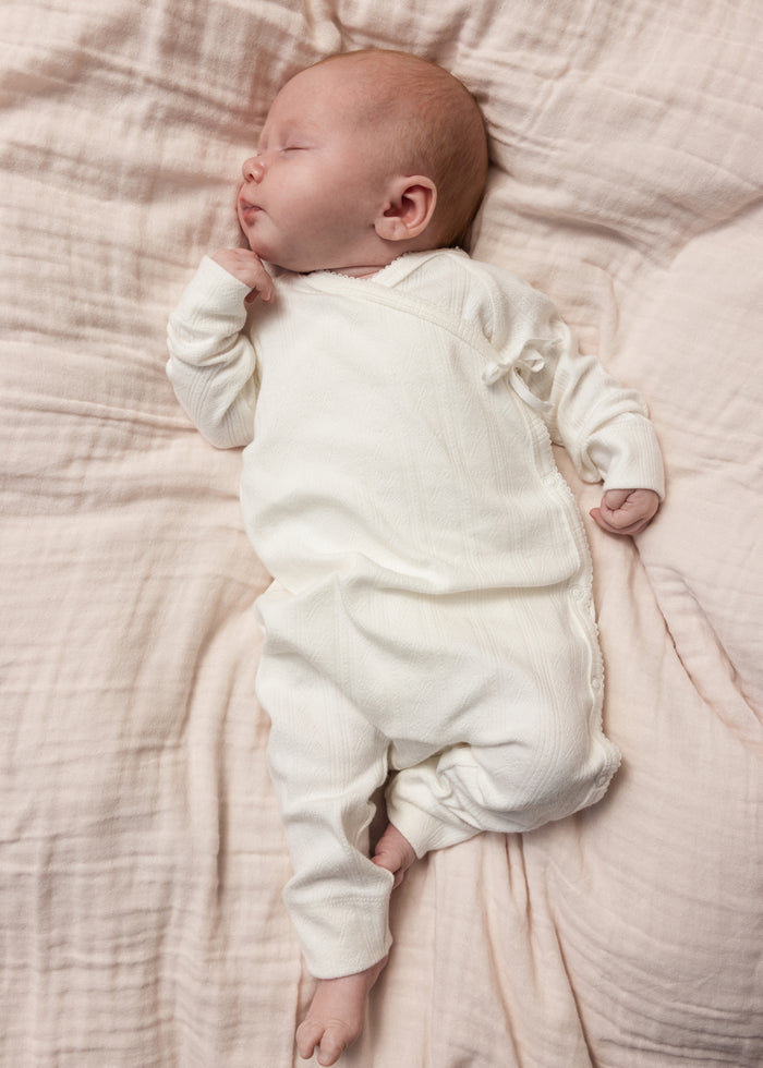 White baby jumpsuit with front snap closure, worn by a sleeping infant.