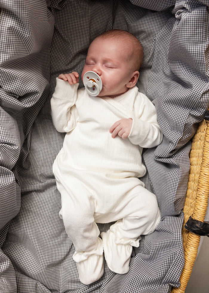 White baby romper with a lace detail at the neckline for infants.
