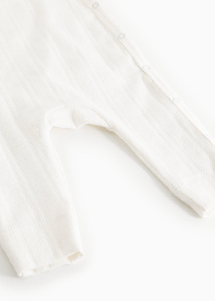 White baby romper with a fine striped pattern and buttons along the front edge.
