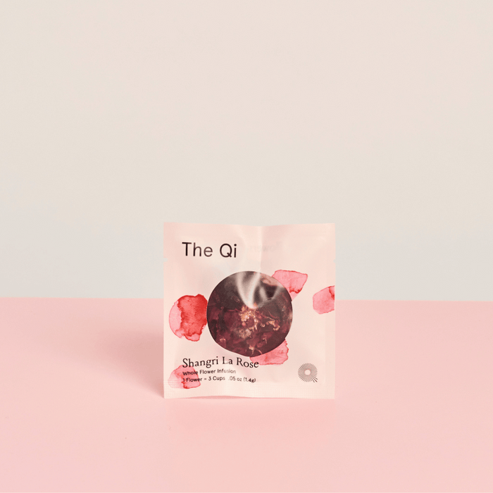 Shangri-La Rose | The Qi tea packet with rose petal design on soft pink and beige background, promoting wellness and body care through a floral infusion.