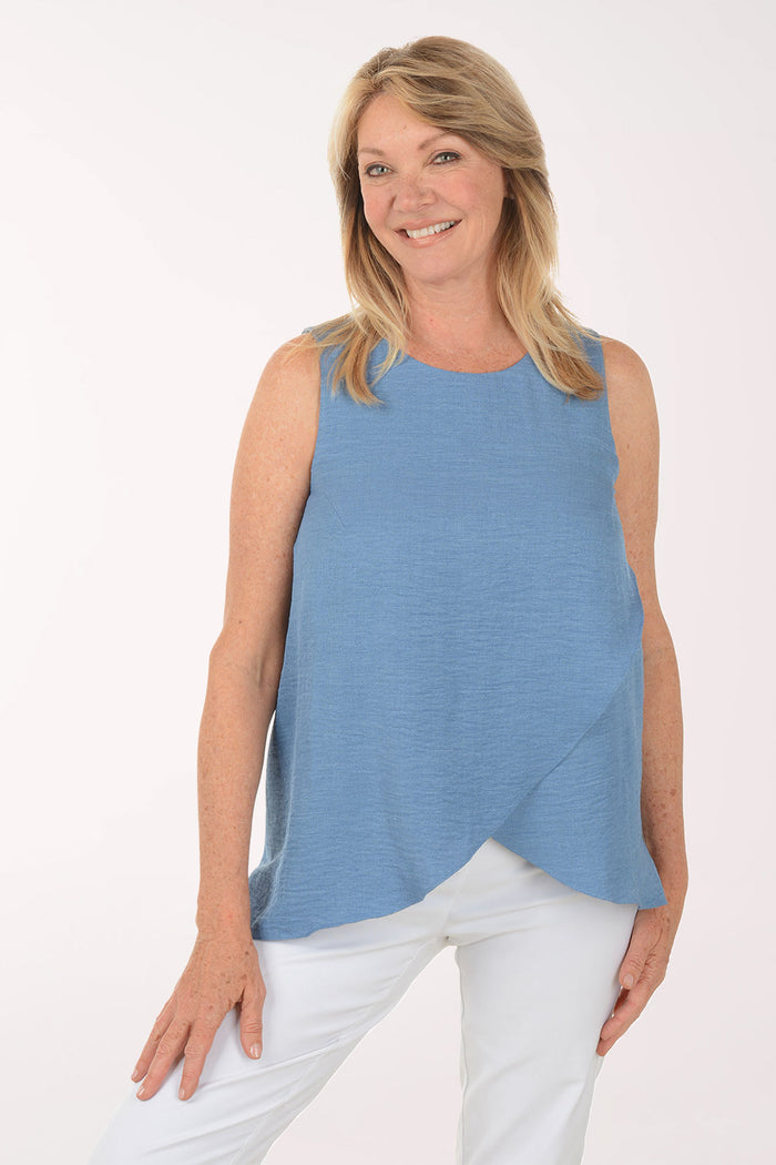 Woman wearing a blue sleeveless top and white pants on a white background