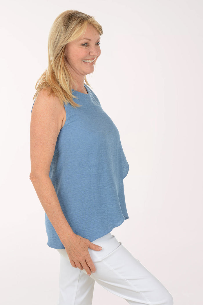 Woman wearing a blue sleeveless top and white pants on a white background
